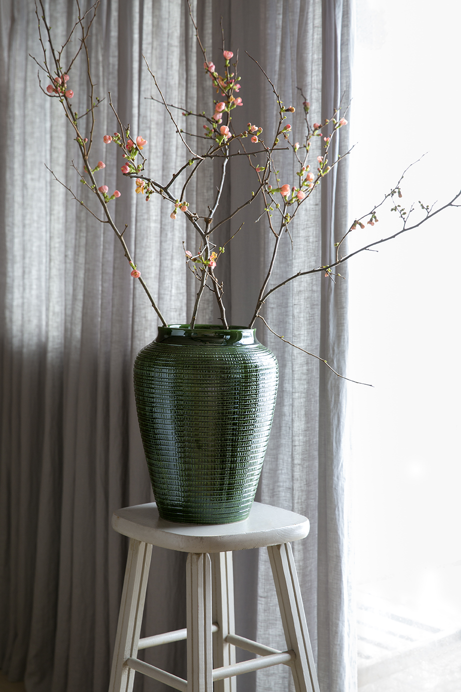 Large glazed green vase with branches on stool