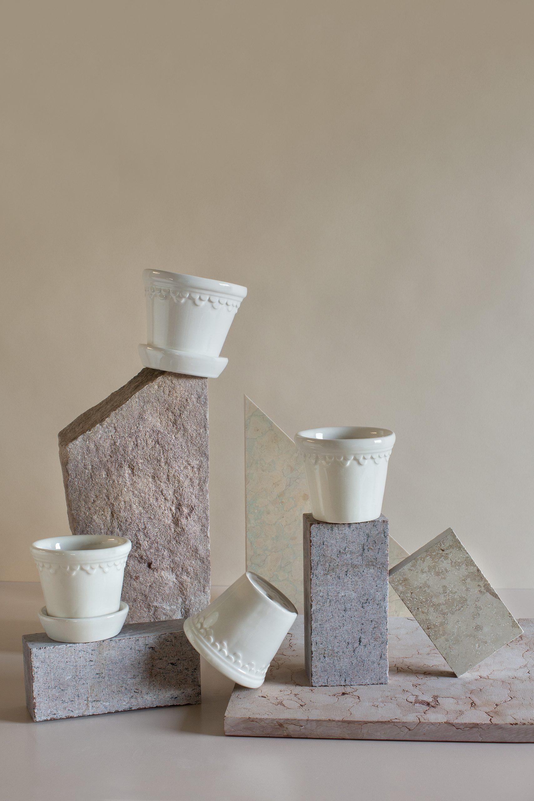 Four glazed white pots are arranged on and around stones.