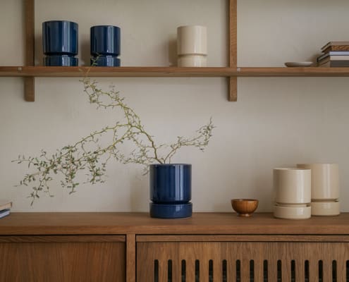 Bergs Potter Hoff pots in deep blue and sandstone styled on a wooden sideboard with books and plants.