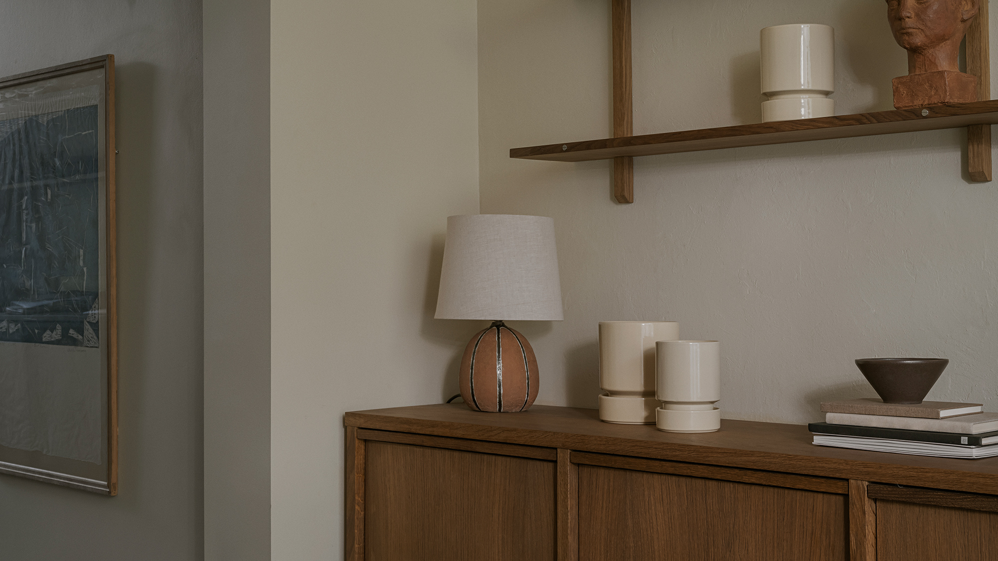 Bergs Potter Hoff pots in sandstone styled on a wooden cabinet with books and a lamp.