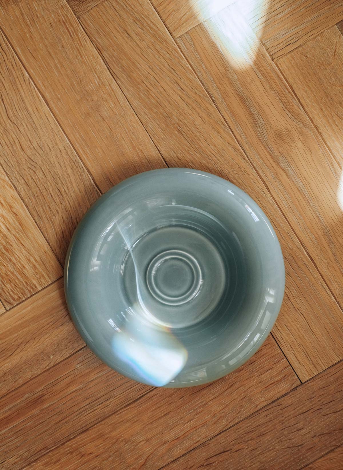 Close-up of Bergs Potter Lily saucer in misty blue glaze on wooden floors