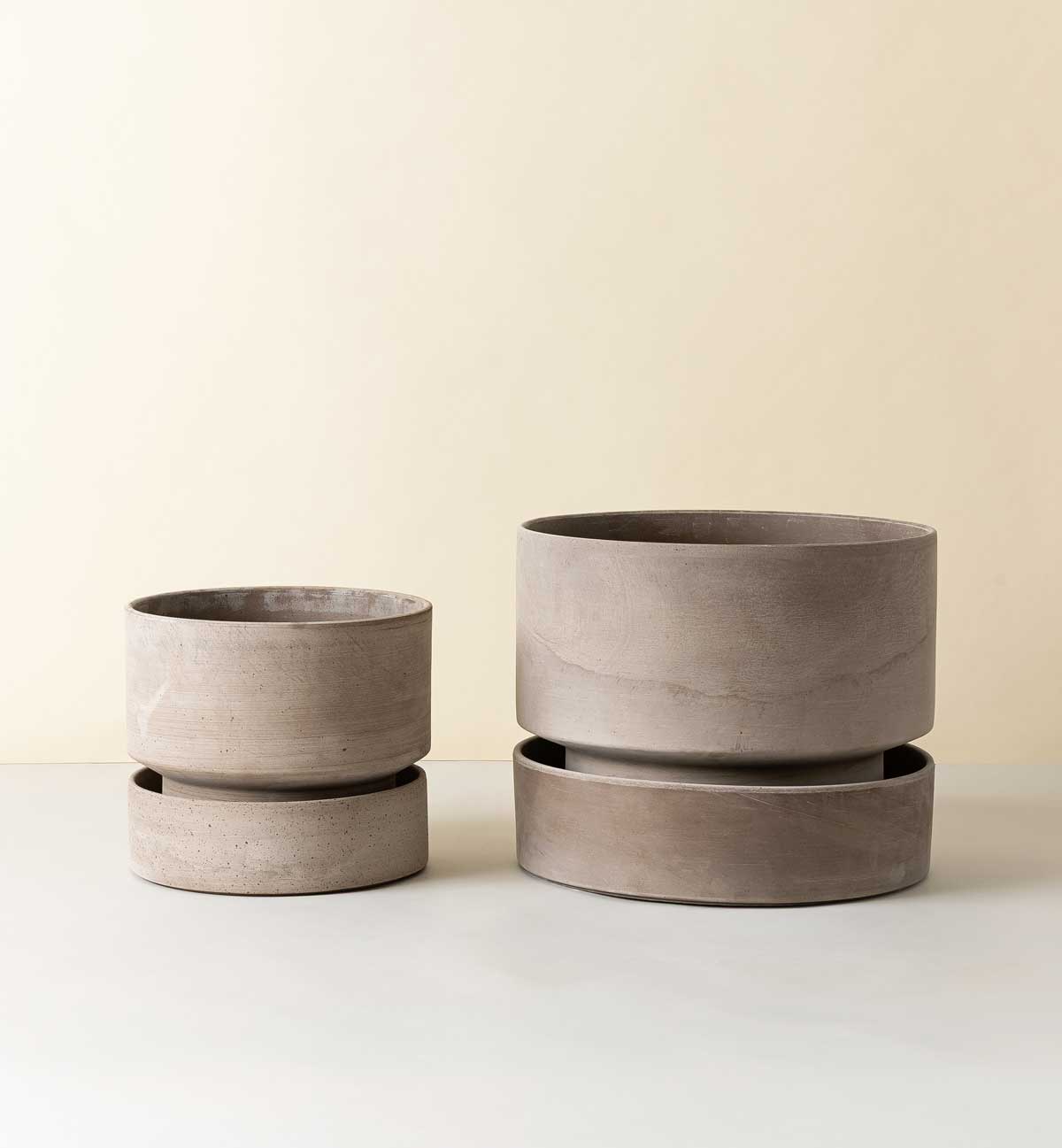 Two Bergs Potter Hoff pots in grey tones, shown in different sizes with matching saucers on a light background.