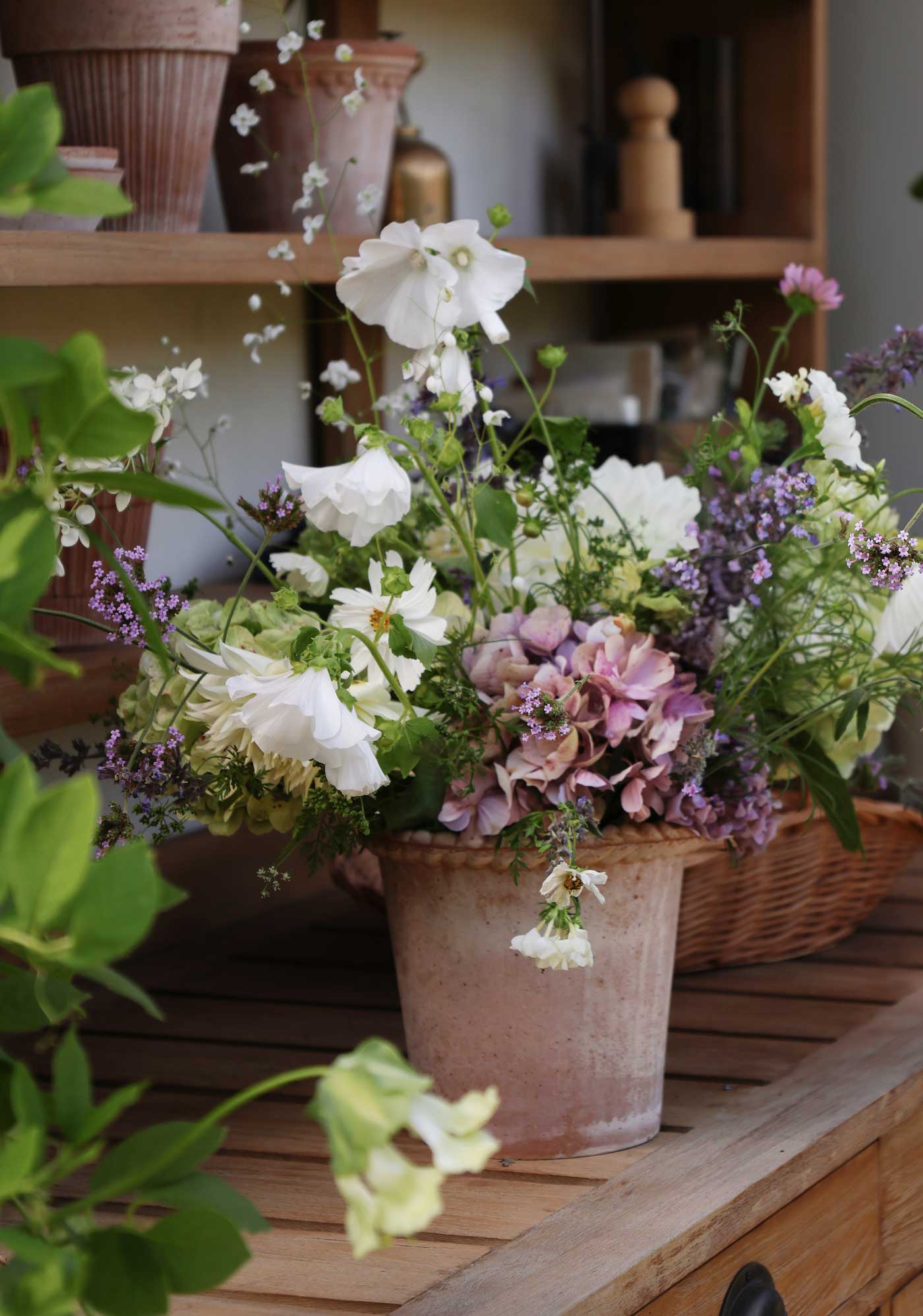 Emilia pot in Rosa terracotta filled with a loose arrangement of white, pink and purple garden flowers, styled on a wooden table.