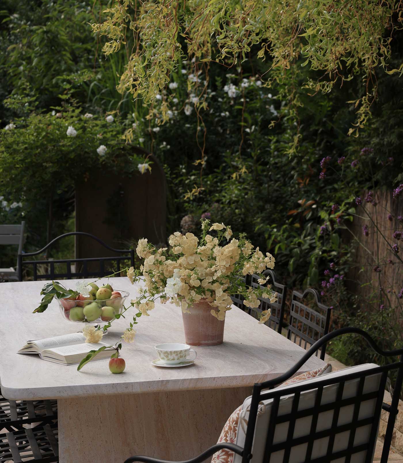 Emilia pot in Rosa terracotta Ø21 styled with pale garden flowers on an outdoor table with apples and a teacup.