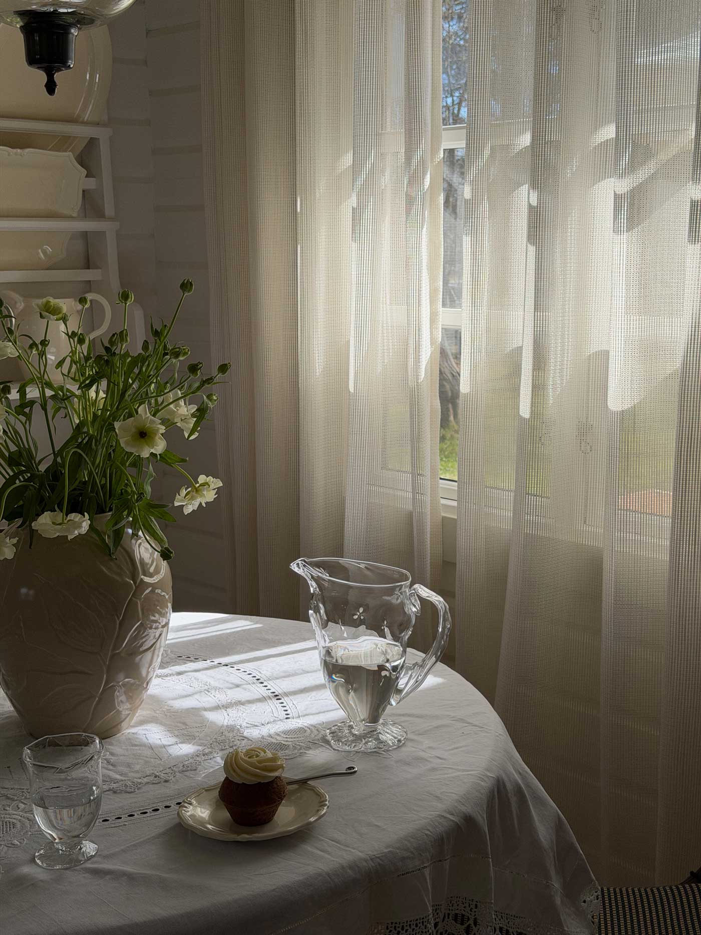 Sunlit table setting in a Danish summer house with white flowers, glassware, a linen tablecloth and soft natural light.